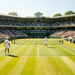 Comment suivre Wimbledon : histoire, traditions et enjeux sportifs ? Vue du Centre Court de Wimbledon sous le soleil, gazon parfaitement tondu et joueurs en tenue blanche, ambiance de tournoi avec un public élégant.