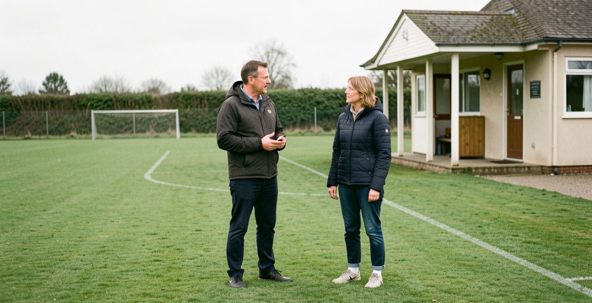 Terrain de football amateur vide avec un adulte référent échangeant calmement avec une parente près du club-house, dans une ambiance protectrice et sereine.